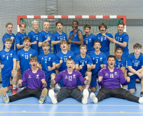 Käsipallojoukkue ryhmittyneenä maalin eteen tuulettaa ja iloitsee joukkuekuvassa